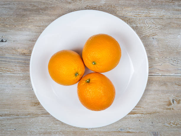 istock Fresh oranges on a white plate on a rustic wooden table close-up.top view 1072298162