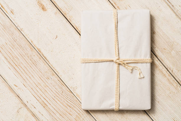 Gift in white wrapping paper on white wooden plank background. Directly above table top shot.