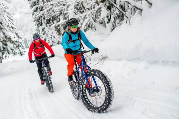 Front view of a mountain biker couple riding their fatbikes up a snowy trail in a forest in winter.