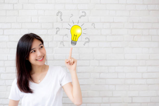 istock Asian woman thinking with drawing question mark for decision and have a idea and finger pointing light on grey cement texture grunge wall brick background, inspiration genius for success concept. 1072313320