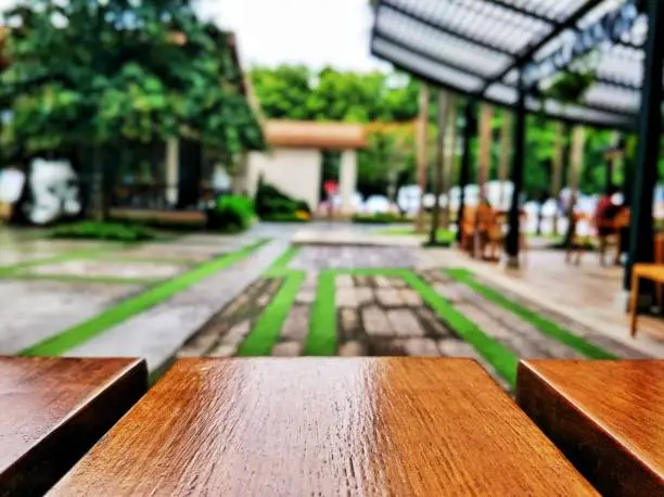 Empty wood board table in front of blurred outdoor dining table and patio