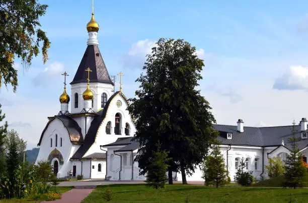 Orthodox Uspensky monastery in the city of Krasnoyarsk. Christian Church in the forest. Church bell. Golden dome in the sun.
