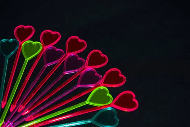 Colorful hearts on black background. Valentine's day. Plastic skewers in the shape of a heart. Decorations for cocktails.