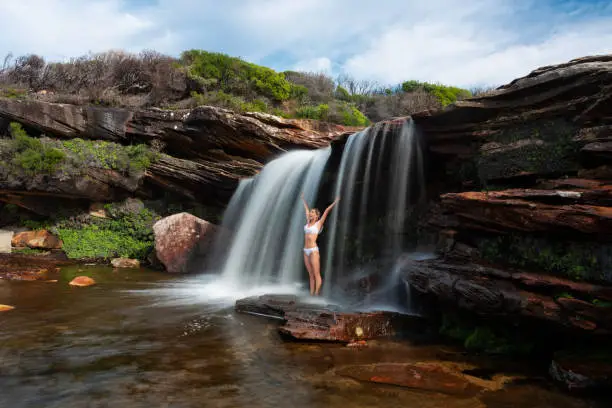 Photo of Female standing under the waterfall flows in bikini