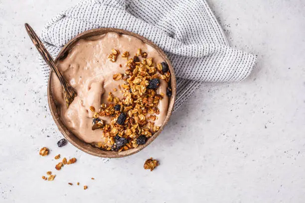 Chocolate smoothie bowl with granola in a coconut bowl, top view. Healthy vegan food concept.