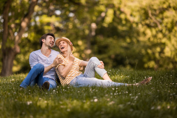 istock Young cheerful couple talking while relaxing in grass at the park. 1072381414