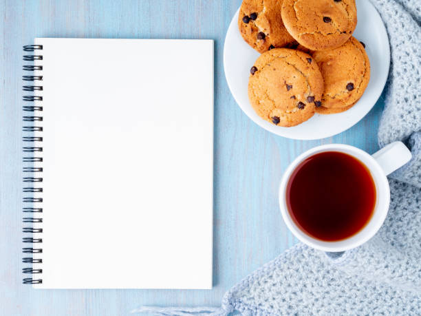istock Mock up with blank Notepad sheet, tea, cookies and knitted warm scarf on blue background, top view, copy space 1072387100
