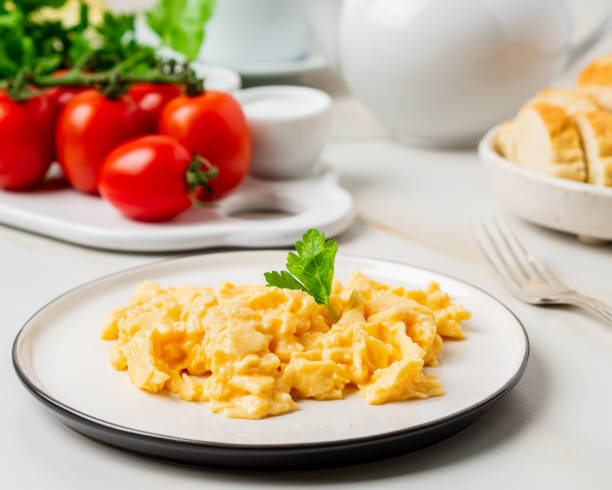 istock Scrambled eggs, Omelette. Breakfast with pan-fried eggs, cup of tea, tomatoes on white stone marble background. Side view 1072387282