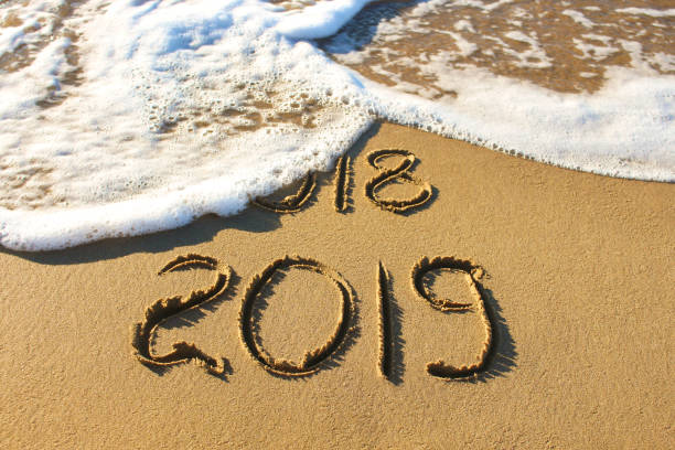 istock 2019, 2018 years written on sandy beach sea. Wave washes away 2017, 2018. 1072395942