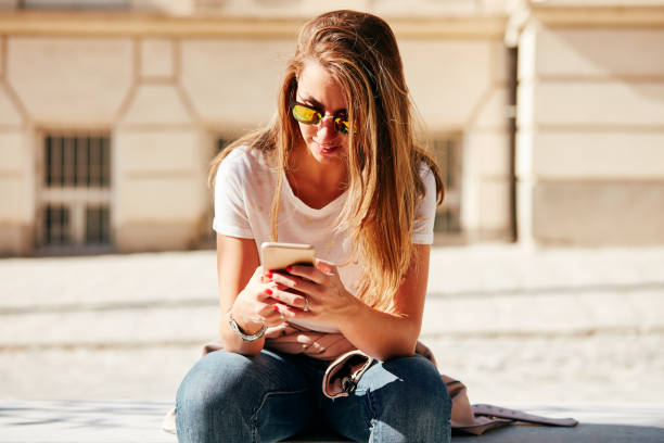 istock Young attractive woman using cellphone while sitting on the bench outdoors. 1072399568