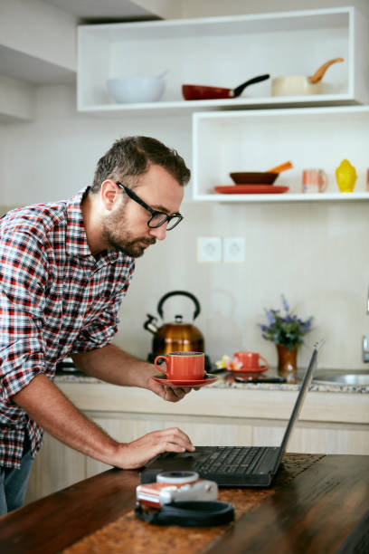 istock Modern bearded man using cellphone and drinking coffee with laptop. 1072401782