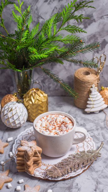 istock A white cup with hot cocoa with marshmallow stands on a gray table among white and gold Christmas ornaments and fir branches 1072420262