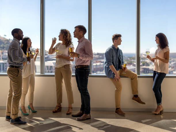 Business people having drinks after successful day. Business people having alcohol at window. Full length of colleagues are talking on corridor after work. Multi-ethnic executives are enjoying in office after successful day. after party stock pictures, royalty-free photos & images