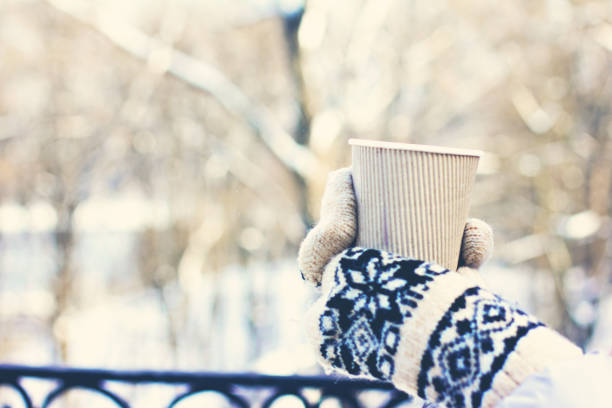 istock Female hands in white and black mittens holding steaming  cup 1072428848