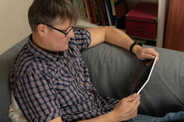 istock A middle-aged man sits on a couch and looks at a tablet's screen with business information. Fithty-something man on a couch holding a tablet with charts and graphs. 1072431362