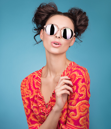 Colorful Studio portrait of a beautiful young woman in sunglasses. A stylish haircut, bright red blouse. Blue background
