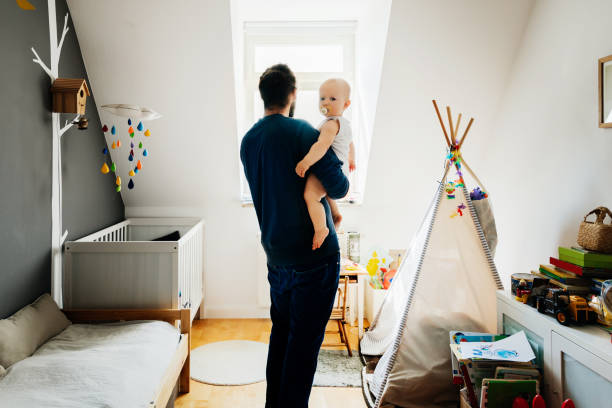 istock Single Dad Looking Out Window Holding His Baby 1072469796