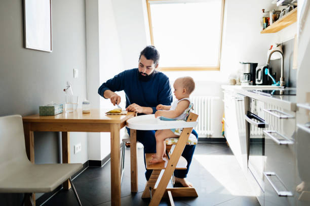 Single Father Feeding Baby In high Chair A single father feeding his baby in a high chair, while at home together in the afternoon. high chair stock pictures, royalty-free photos & images