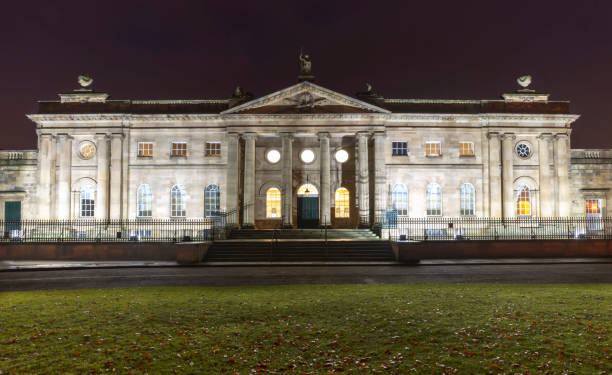 York Crown Court building at dawn.  The lawn in the foreground is covered in leaves, while the building is illuminated. A dark dawn sky is overhead.