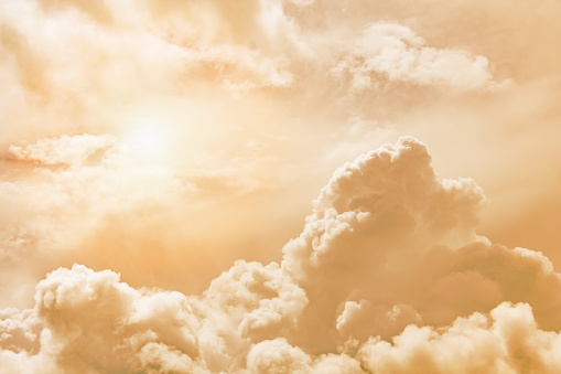 Fluffy clouds illuminated by the sun against a orange sunset sky (background, toned)