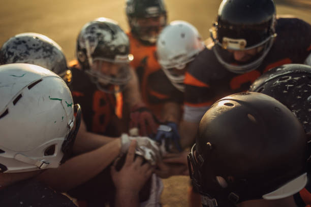 Group of men, American football team on training outdoors, holding hands all together.