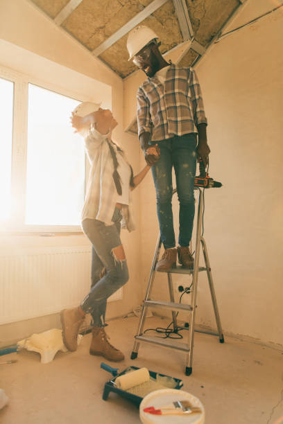 istock low angle view of man in hard hat and goggles standing power drill on ladder while his girlfriend standing near during renovation of home 1072496874