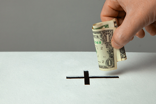 Man puts donation in his hand with dollar in slot in the form of Christian cross. Copy space for text.
