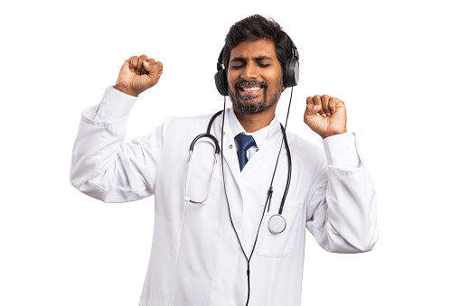 Indian medic man dancing with hands up and eyes closed on music in headphones enjoying himself isolated on white
