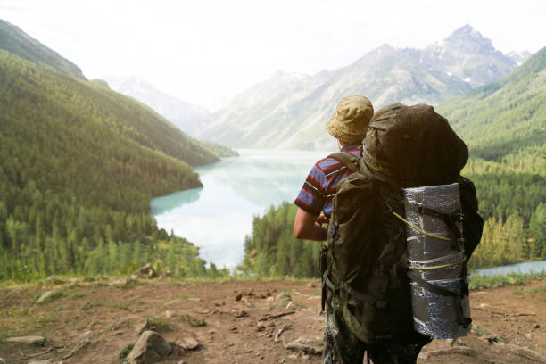 A man traveler stands on top of a mountain and looks into the distance on a clear lake.