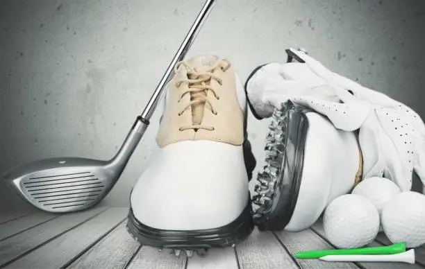 A pair of golfing shoes and a golf club on  background