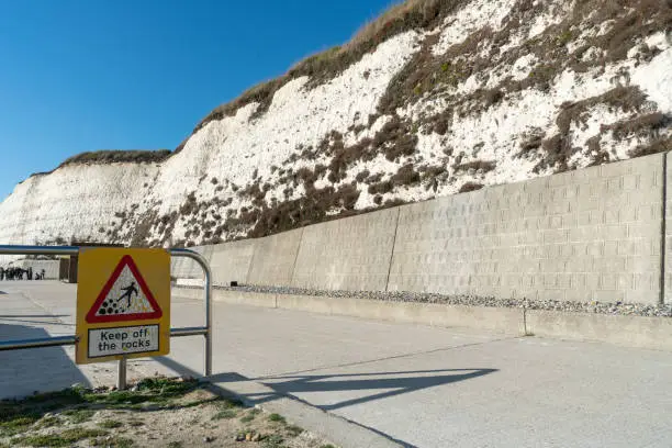 Photo of Warning, danger, alert sign rocks fall at Saltdean beach seafront and white sandstone chalk cliffs.