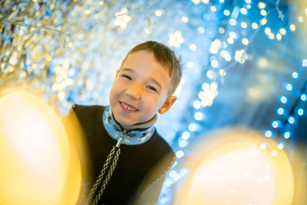 Happy cute boy the elementary age is smiling with toothy smile and looking at the camera. Studio shooting at holiday Christmas lighting with defocused bokeh light. A shining glittering glowing background