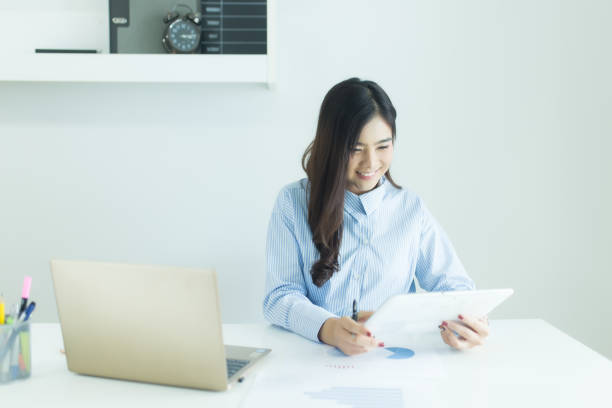 istock Young asian business woman using tablet for working at desk in office with documents and laptop 1072539400