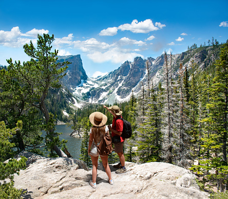 Couple relaxing and enjoying beautiful mountain view. Man and woman with backpacks looking at Dream Lake.Early summer landscape with lake  and snow covered mountains.Rocky Mountains National Park, USA