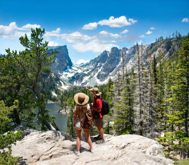 Couple relaxing and enjoying beautiful mountain view in Colorado. Couple relaxing and enjoying beautiful mountain view. Man and woman with backpacks looking at Dream Lake.Early summer landscape with lake  and snow covered mountains.Rocky Mountains National Park, USA rocky mountain national park photos stock pictures, royalty-free photos & images