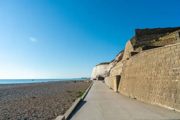 Photo of Saltdean beach seafront and white sandstone chalk cliffs with two local people walking for exercise.