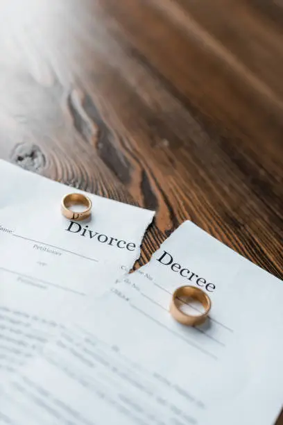 Photo of close-up shot of teared divorce decree and engagement rings on wooden tabletop