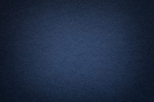 Texture of vintage dark denim paper background with vignette. Structure of dense navy blue kraft cardboard with frame. Felt gradient backdrop closeup.