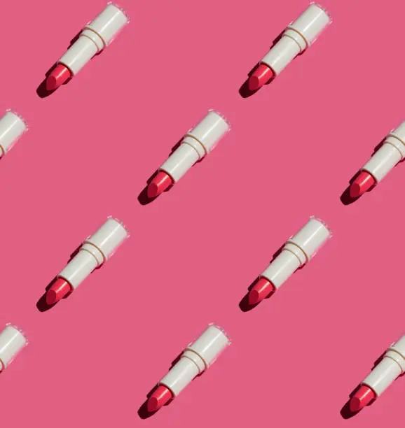 Photo of Seamless pattern of red tinted balm lipstick flat lay on pink paper.