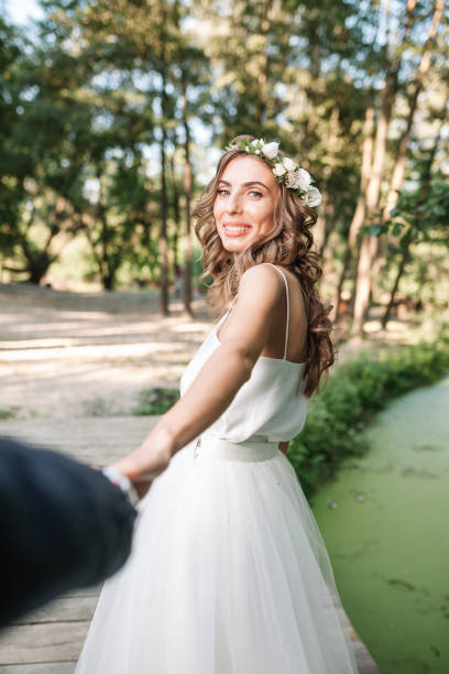 suis-moi mon concept de l’amour. belle jeune femme habillée en robe de mariée blanche tenant la main de son copain et la marche sur le beau jardin d’avenir heureux - wedding suit photos et images de collection