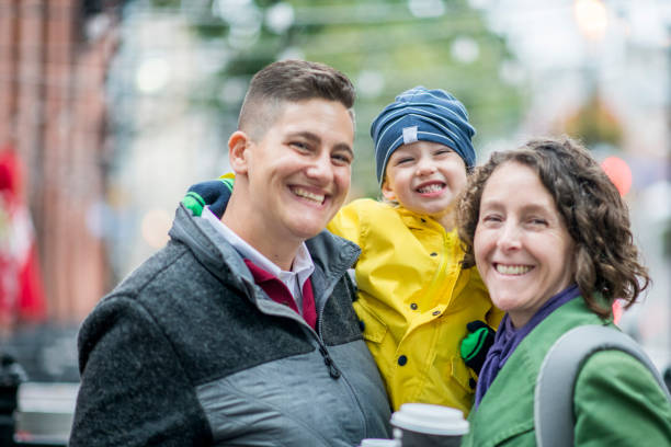 Parents And Child Two lesbian women and their son are smiling happily at the camera on a rainy day. gay pride symbol photos stock pictures, royalty-free photos & images
