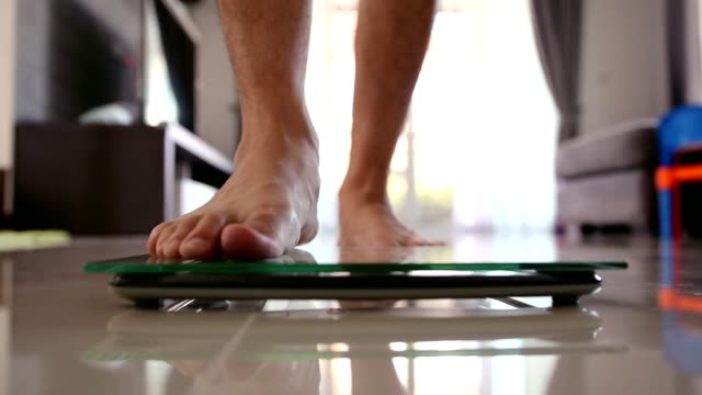 Close up men barefoot legs stepping on flooring scales for weighting in living room.