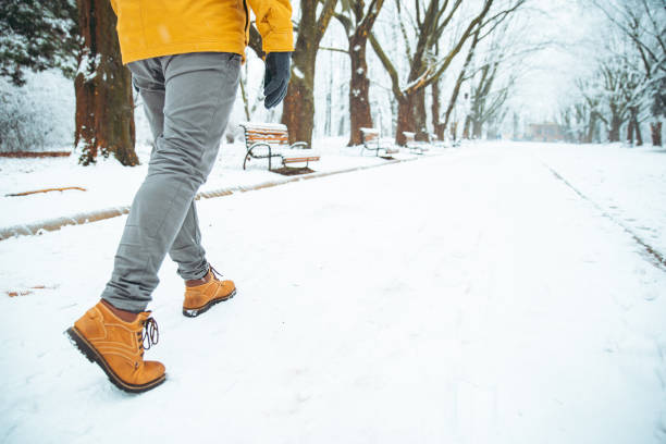 雪が降った冬都市公園の足で歩み行く男をクローズ アップ - snow winter bench park ストックフォトと画像