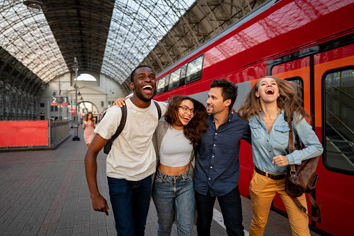 Group of friends traveling by train and looking very happy laughing at the platform - transport concepts