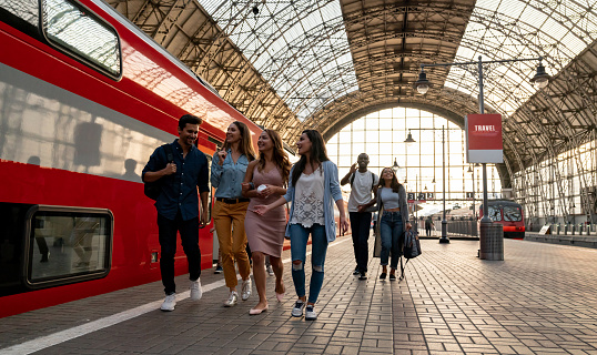 Happy group of friends traveling by train and walking to the platform â rail transport concepts