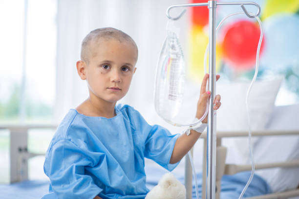 Sitting with IV A young boy with a shaved head is sitting on a hospital bed. The boy has cancer, and he is attached to an IV. He is staring at the camera. sick child hospital bed stock pictures, royalty-free photos & images