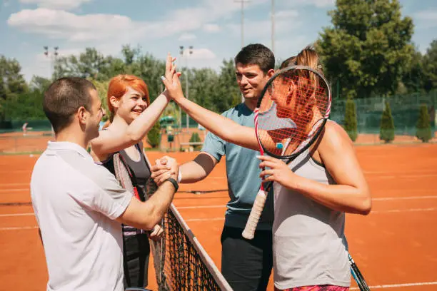 Four young friends giving a high-five after tennis training. Selective focus.