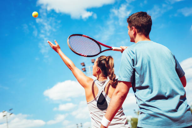 Girl Practice Tennis With Coach Beautiful young left-handed woman with her trainer practicing serve on outdoor tennis court. tennis coach stock pictures, royalty-free photos & images