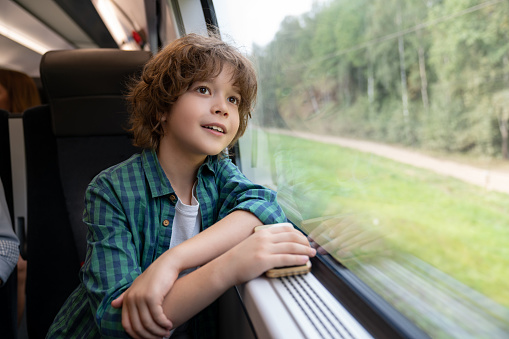 Portrait of a happy boy traveling by train and looking through the window â rail transportation
