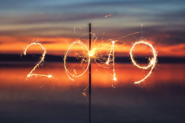 istock 2019 happy new year written with Sparkle firework on sunset background 1072621062